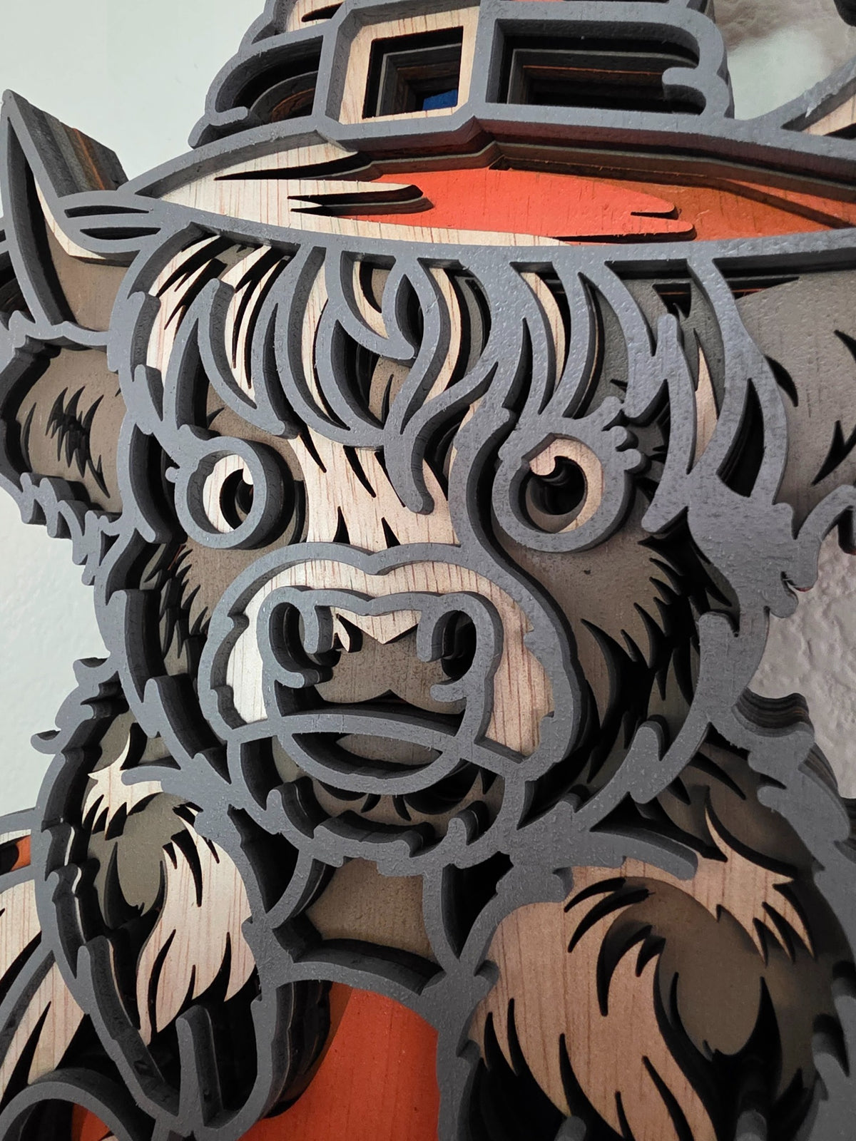 Close-up detail of Highland cow face and witch hat on layered wooden Halloween wall art