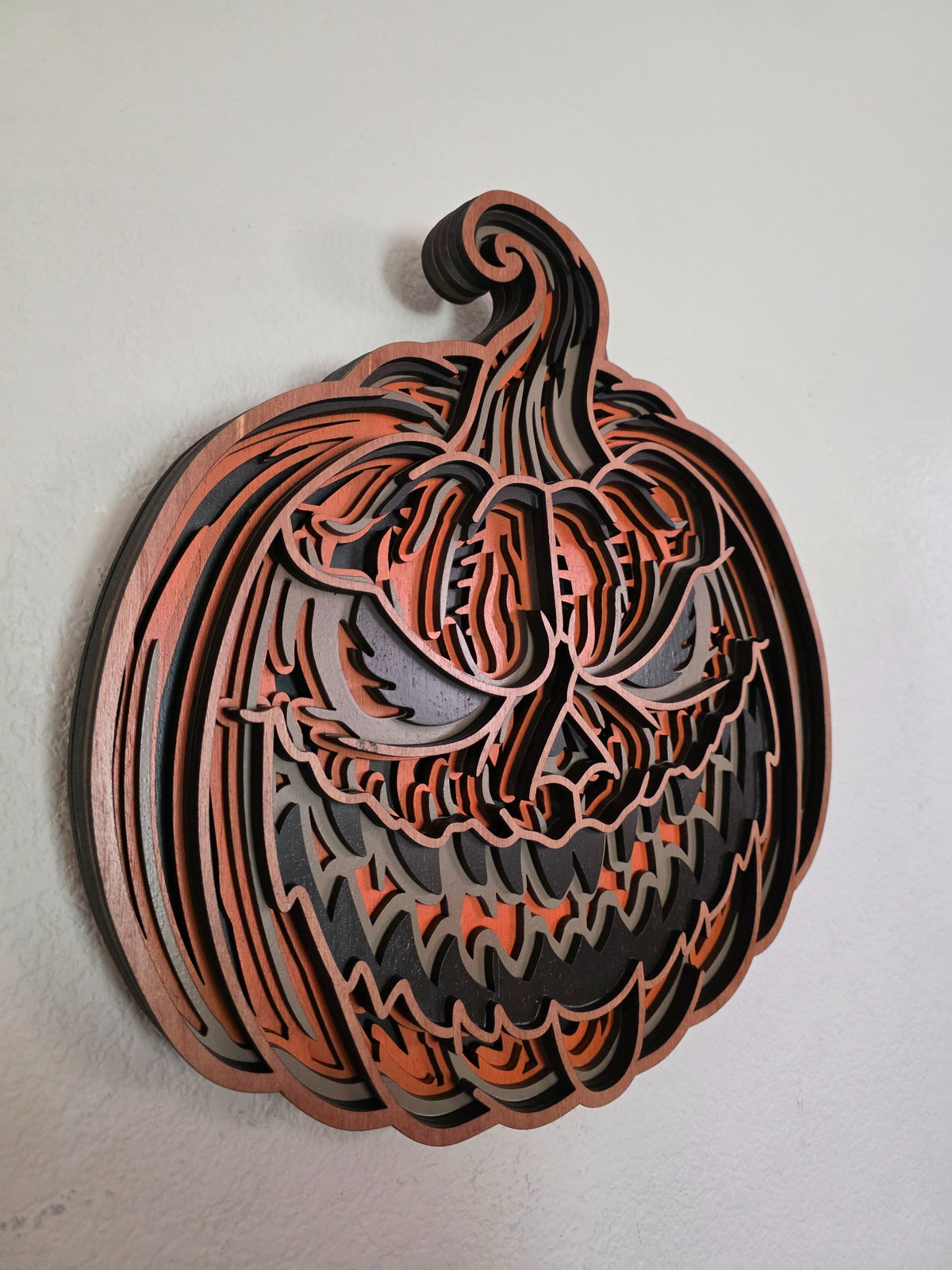 Angled view of sinister layered wooden jack-o-lantern pumpkin wall art showing dimensional wood layers